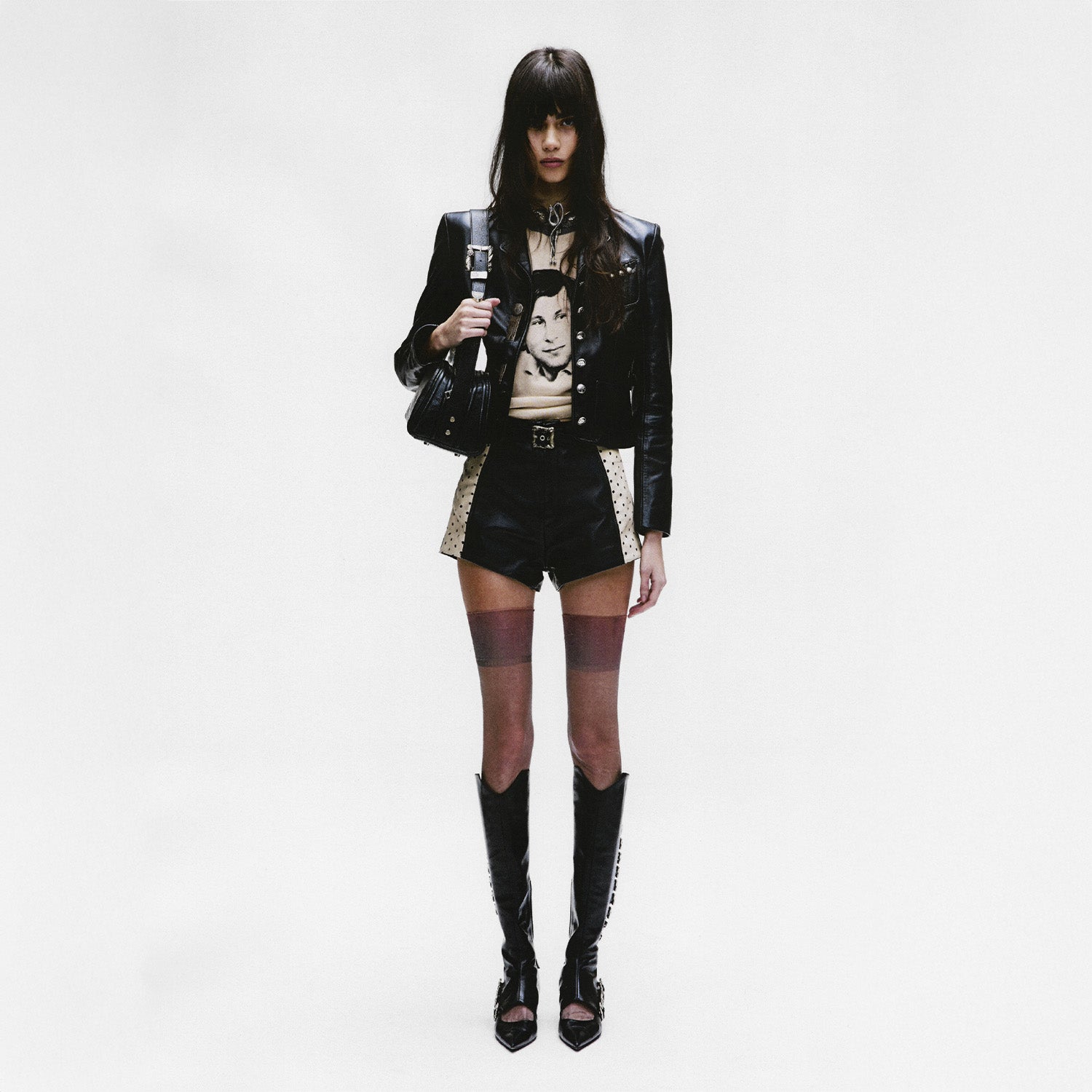 Person wearing a black leather enfants riches deprimes jacket, black shorts, and black knee-high boots on a white background