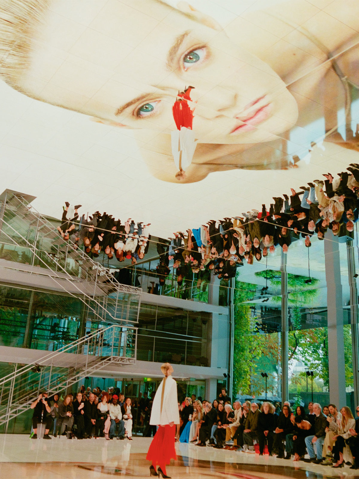 Large indoor event with people, a central figure in a red skirt, and a large ceiling installation. The Alaïa fashion show.