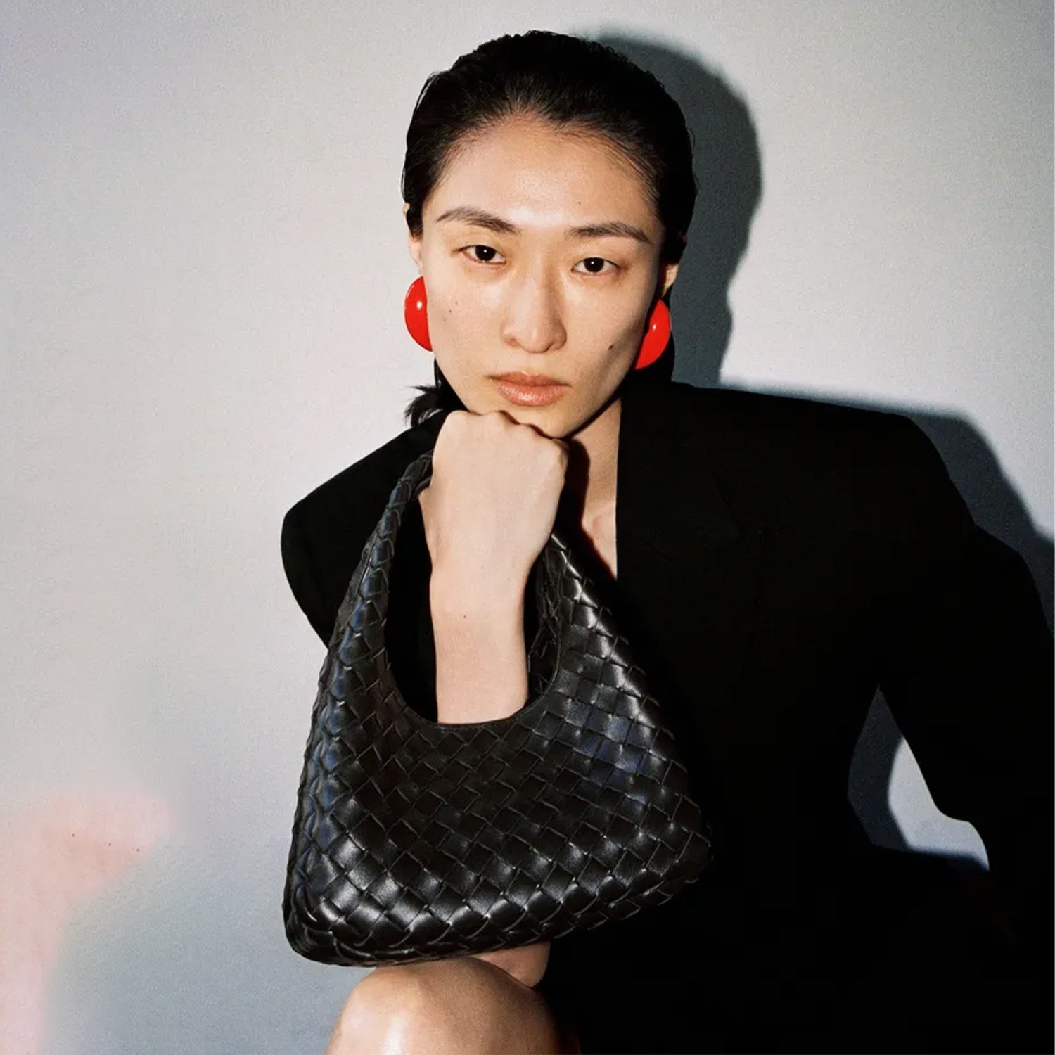 Woman holding a black woven Bottega Veneta handbag against a plain background