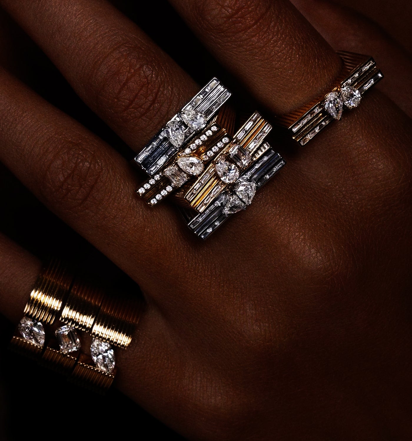 Close-up of a hand wearing multiple Loraida diamond rings with a dark background