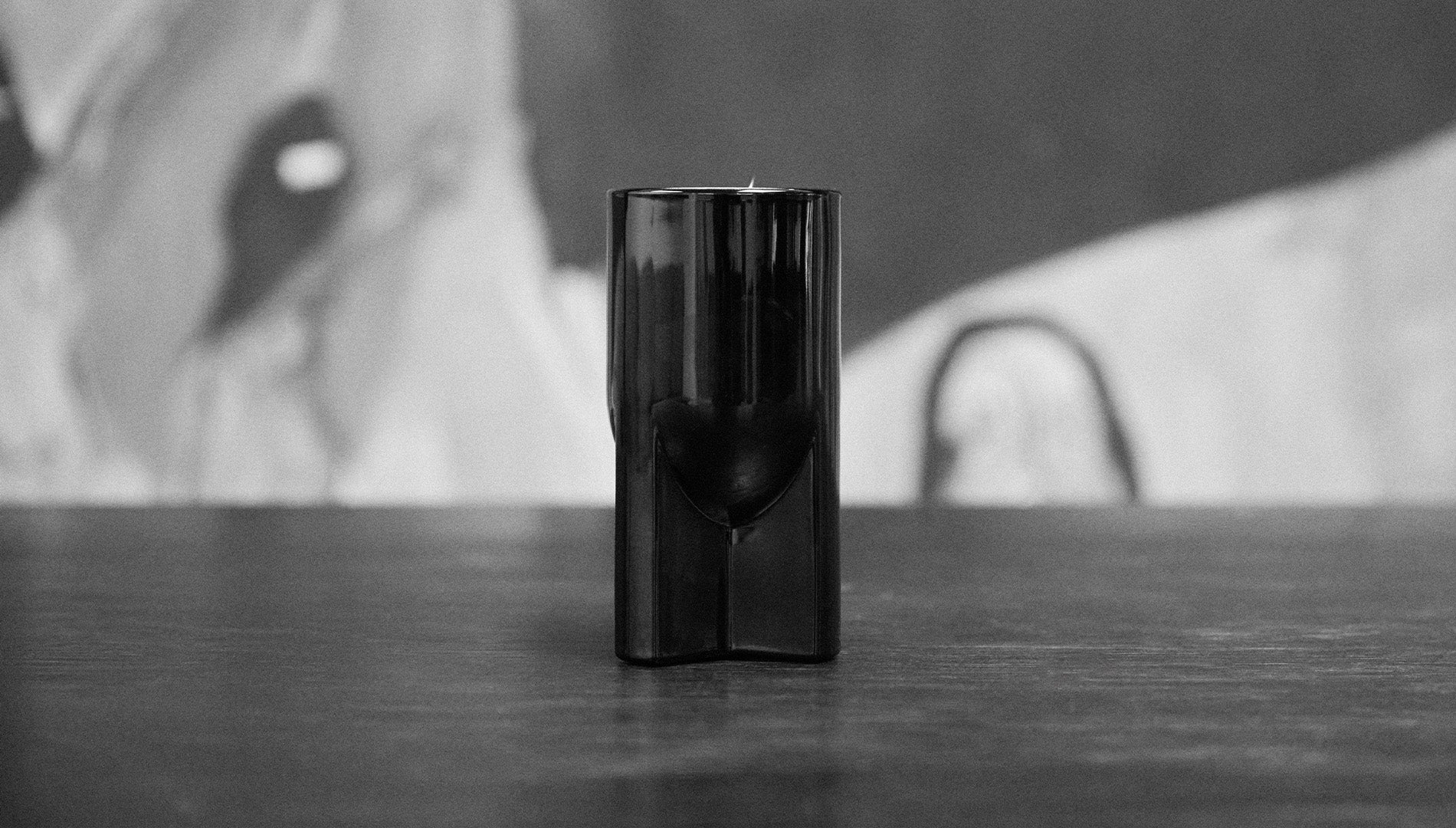 Black cylindrical Rick Owens Candle on a reflective surface with a blurred background