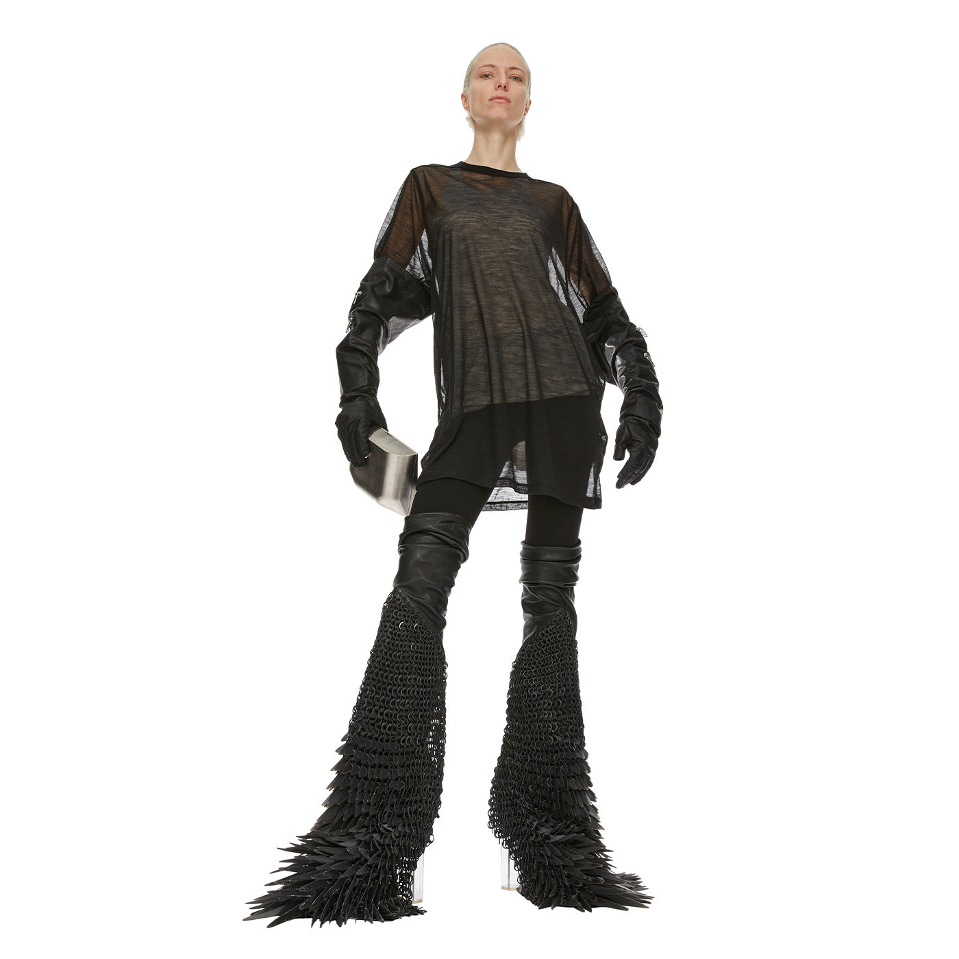 Person wearing a Rick Owens black outfit with sheer sleeves and feathered boots on a white background