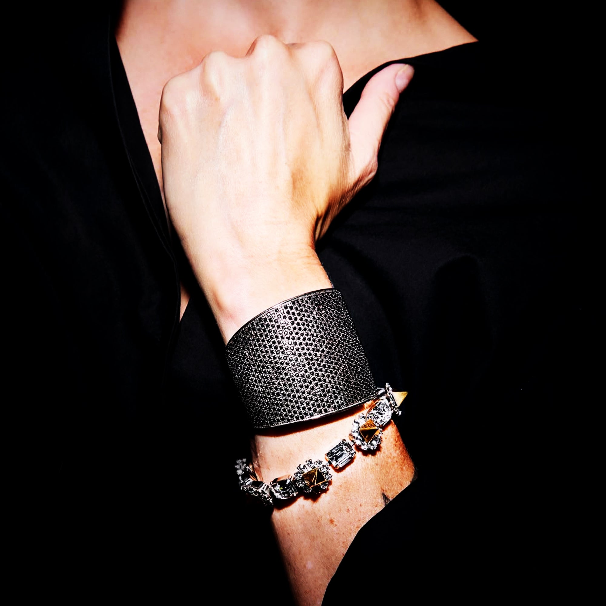 Person wearing a black textured Tom Binns bracelet on a dark background
