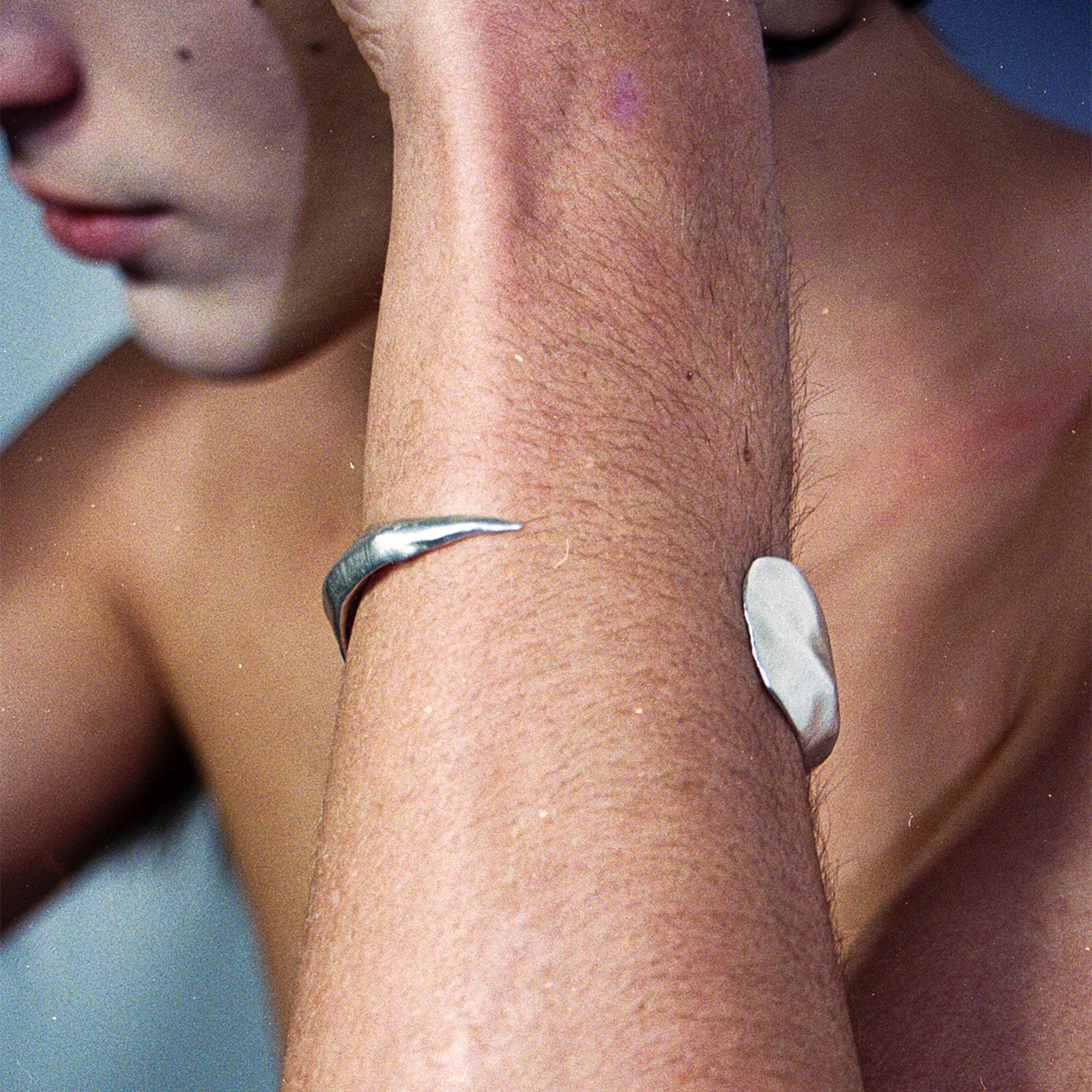 Close-up of a person's arm with a silver ring and a white bandage on a blue background