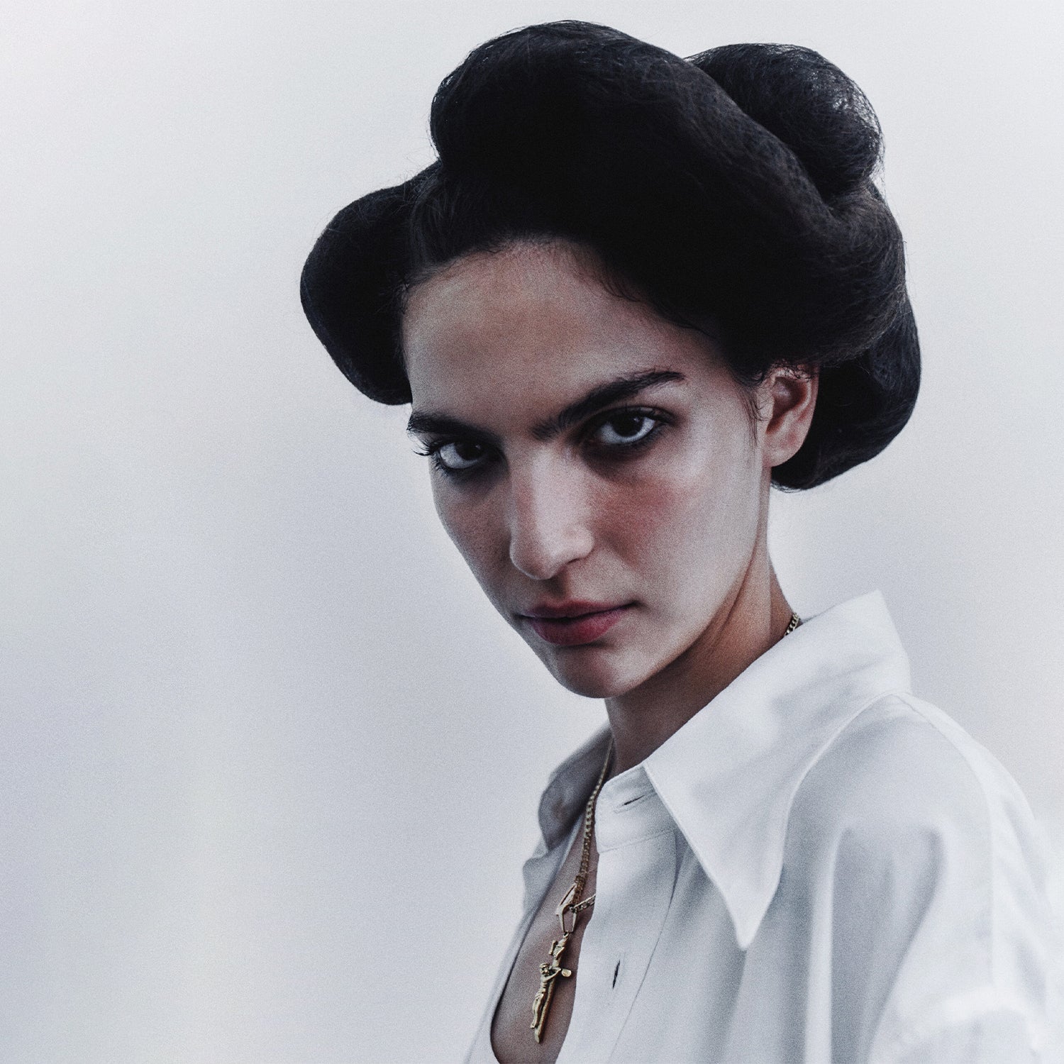 Model on a stark white background wearing gold jewelry and Willy Chavarria with cool hair style.