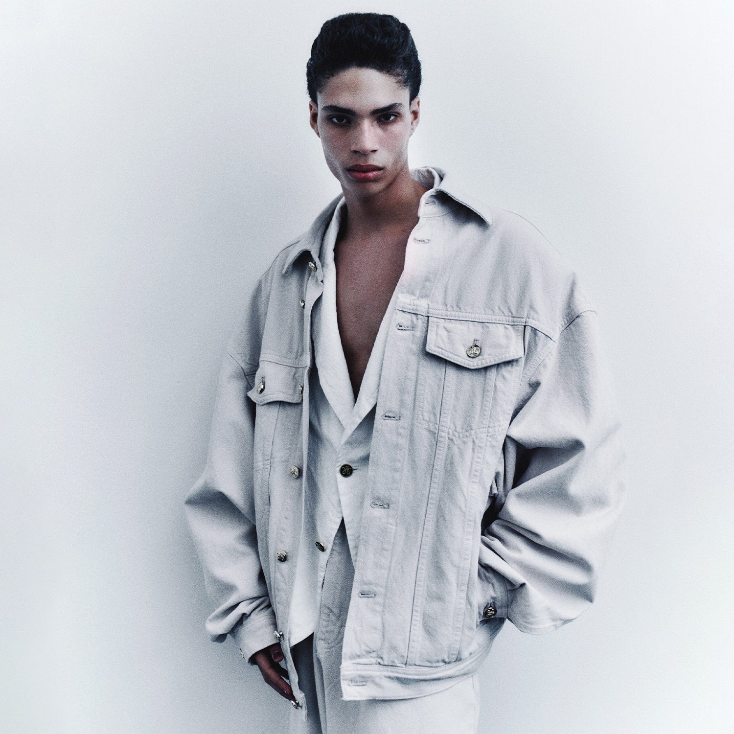 Model on a stark white photoshoot wearing grey denim Willy Chavarria jacket.